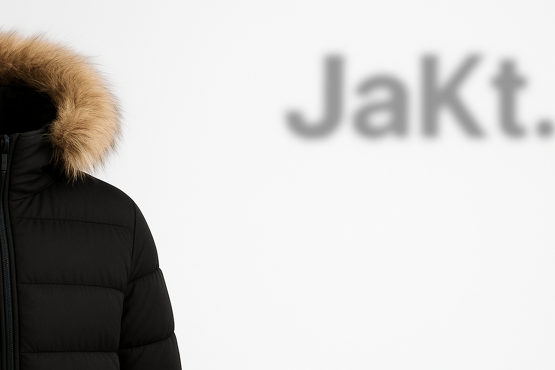 Black puffer jacket with fur hood on a white background with 'JaKt.' branding.